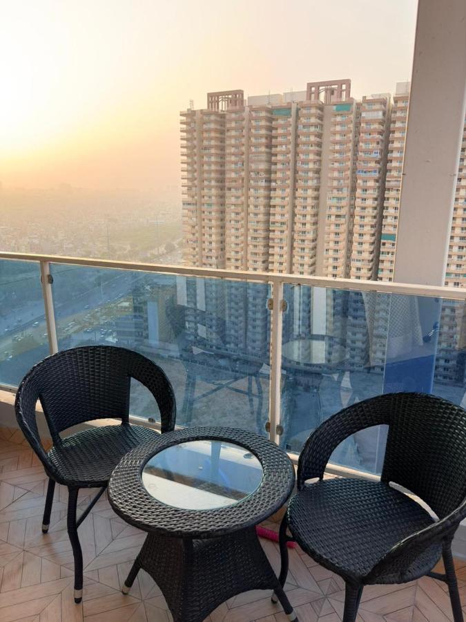 Private balcony with two wicker chairs and a glass-top table overlooking high-rise towers at sunset