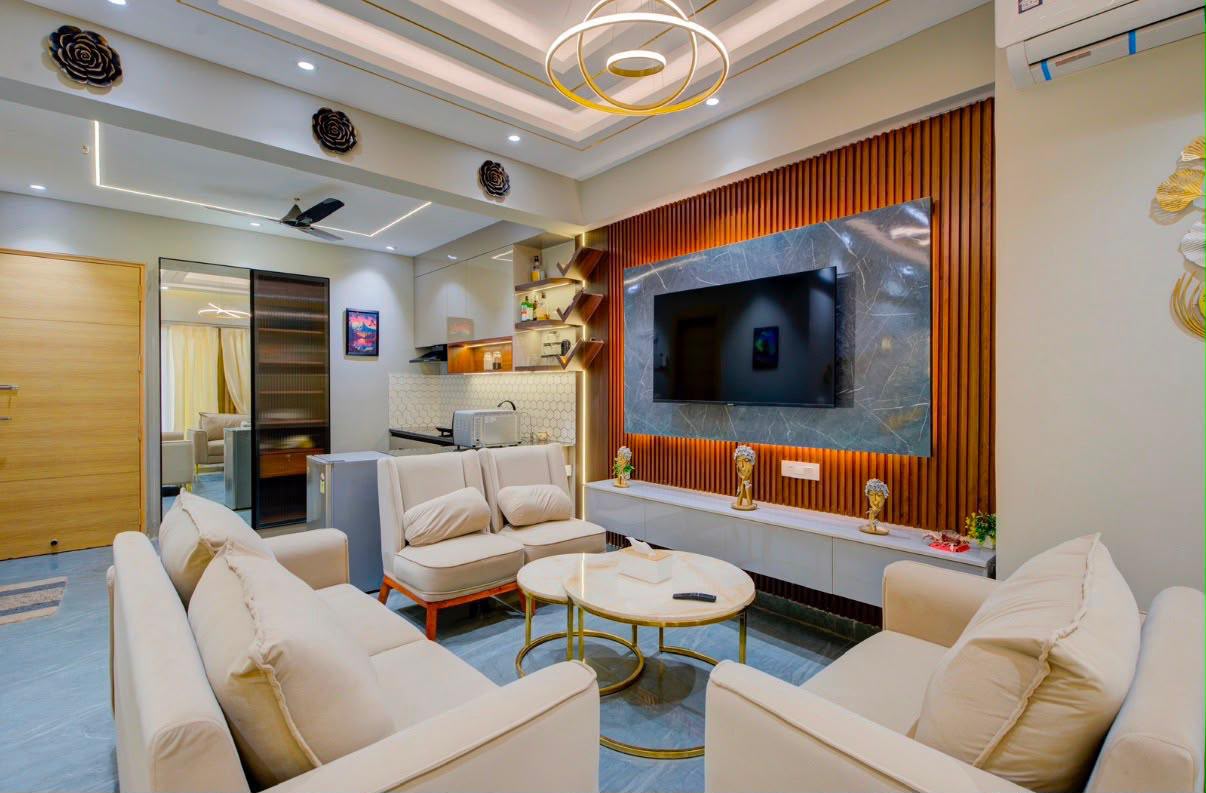 Studio living area with cream sofas, a marble-look and wood-slat TV wall, and a kitchenette in the background